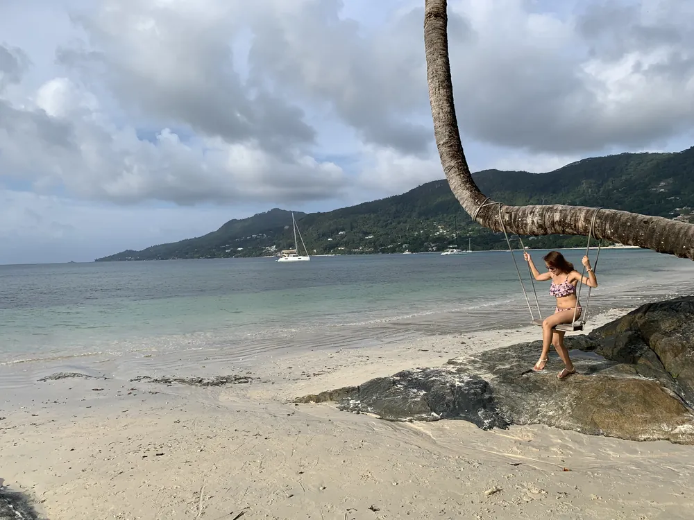 Dee on a rope swing hanging from a palm over the beach
