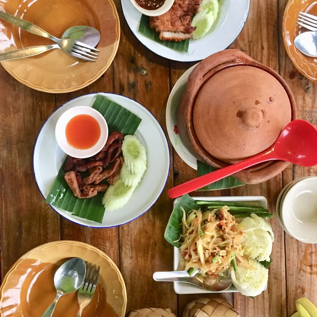 A table of som tam, crispy pork, dipping sauces and a clay pot