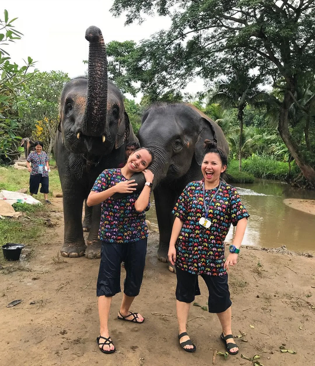 Dee and Kimy laughing with two elephants by the river