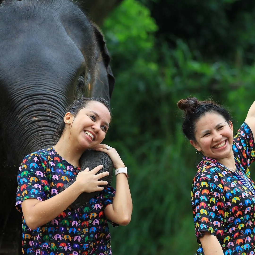 Dee hugging an elephant’s trunk, with a friend smiling beside her