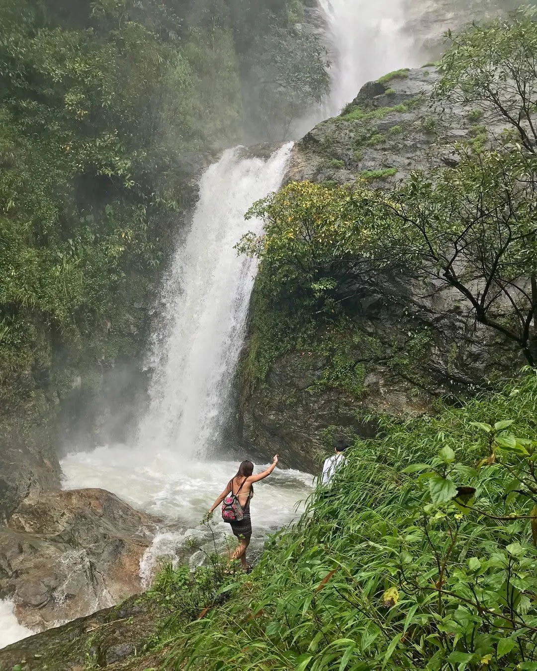 Dee reaching out toward a tall waterfall in the misty jungle