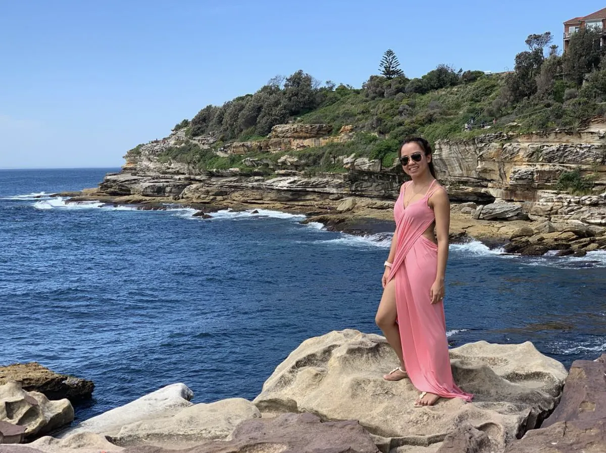 Dee in a long pink dress on sandstone rocks above the sea