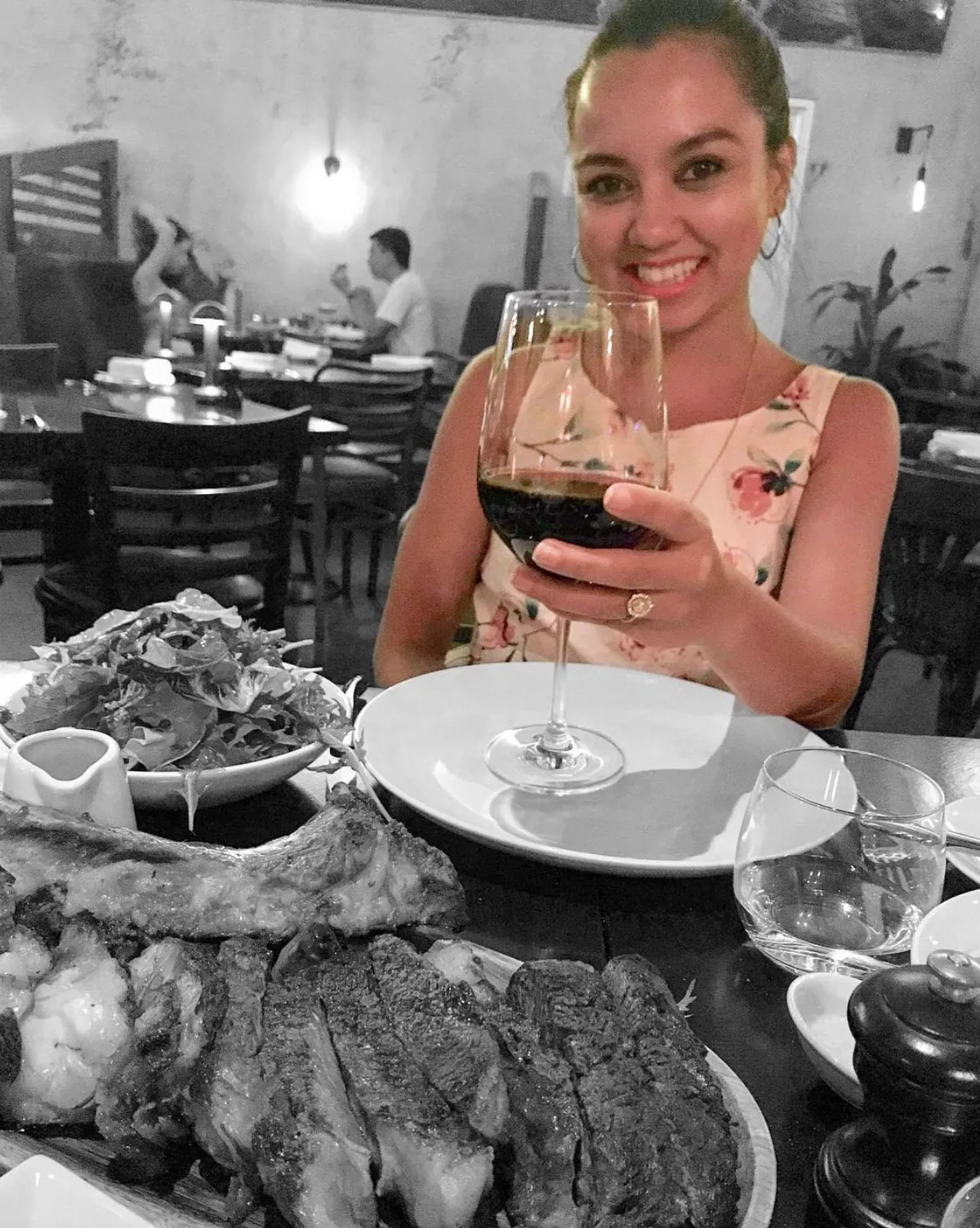Dee raising a glass of red wine over a steak dinner