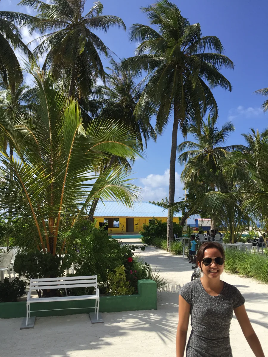 Dee smiling on a sandy, palm-lined path on Maafushi