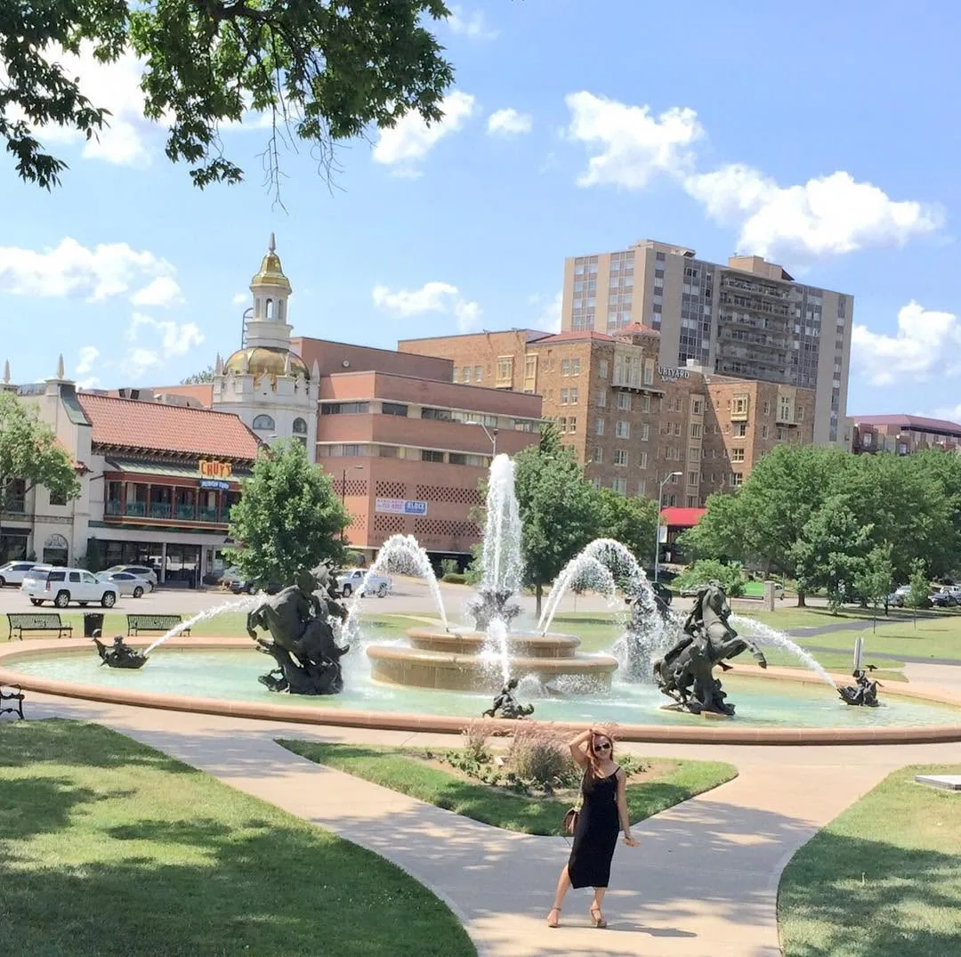 Dee in a black dress by a fountain with bronze horses