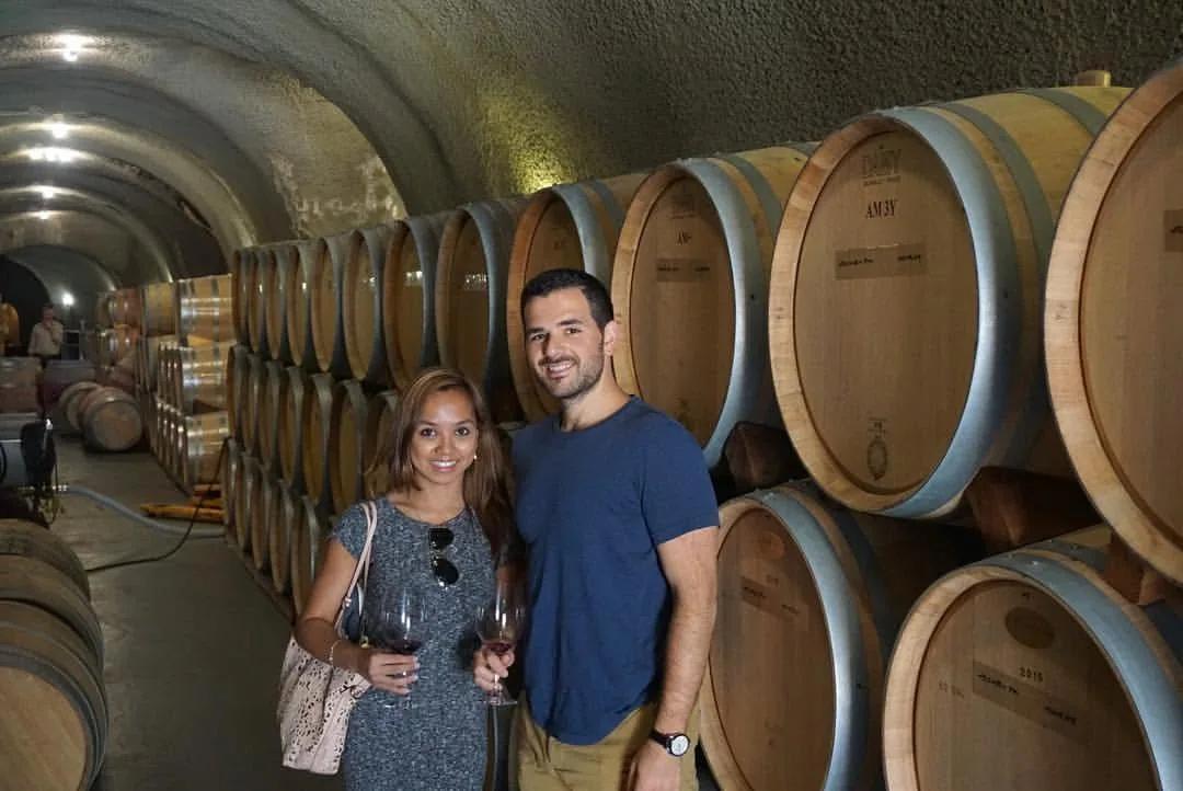 Dee and her husband holding wine glasses in a barrel cellar