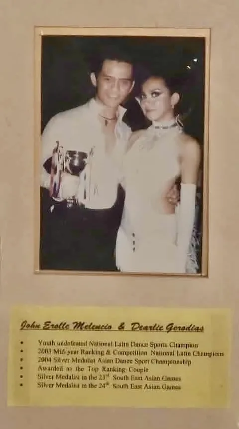 Close-up of a photo of Dee and John Erolle with a trophy, above a list of their titles