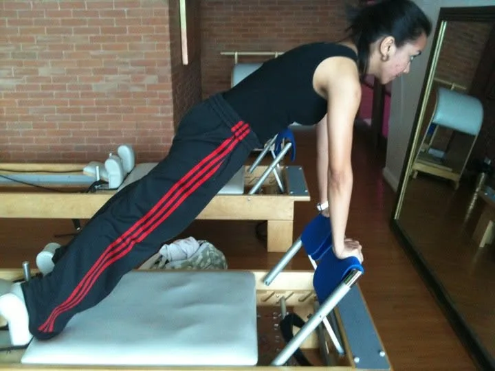 Dee in a plank position on a Pilates reformer