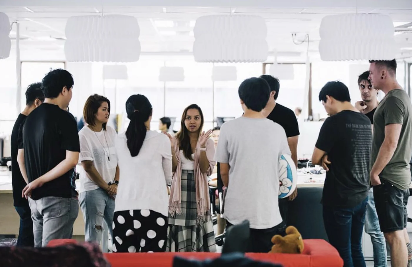 Dee leading a daily stand-up with her team of designers, testers and engineers in a bright open-plan office