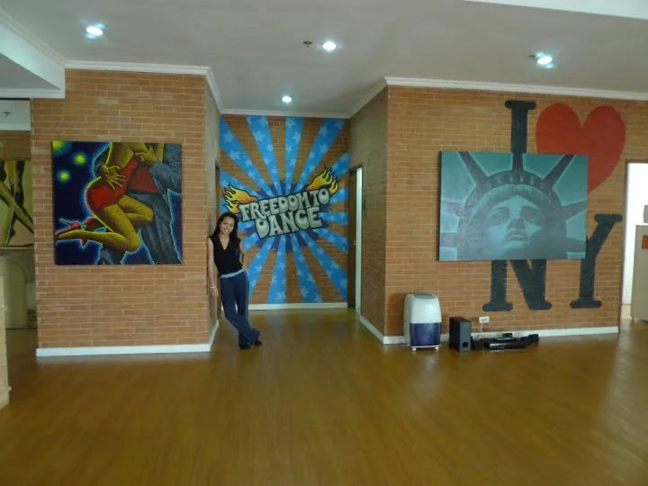 Dee standing in a dance studio with brick walls, wooden floors and colourful murals