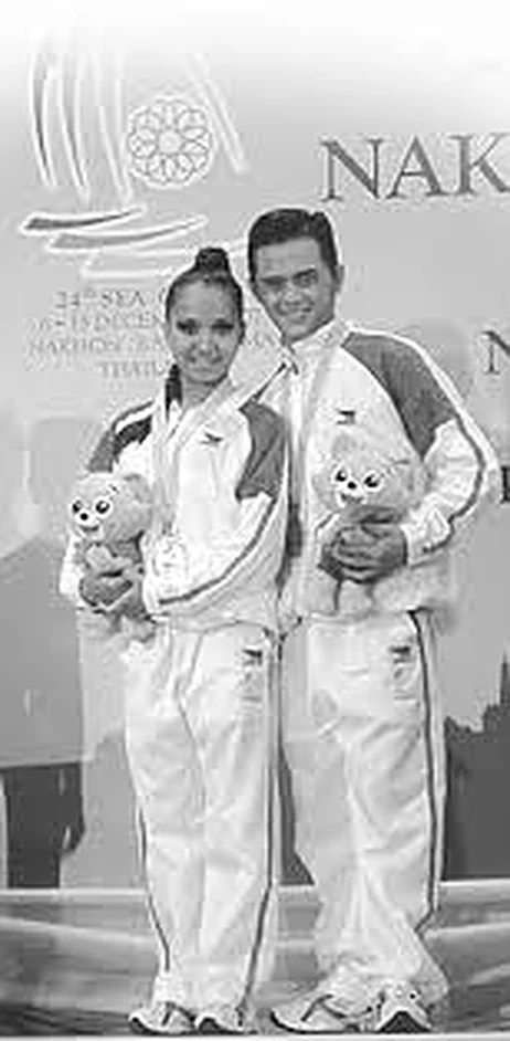 Dee and John Erolle in Team Philippines tracksuits holding mascots on the podium at the 24th SEA Games in Nakhon Ratchasima, Thailand